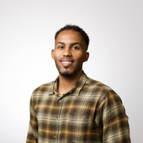 A professional headshot of Kevin Saruni Tipatet smiling wearing an earth toned plaid button up shirt.