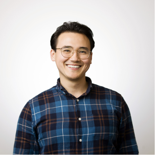 A professional headshot of Dr Jani Shibuya smiling wearing a blue and red plaid button up shirt.